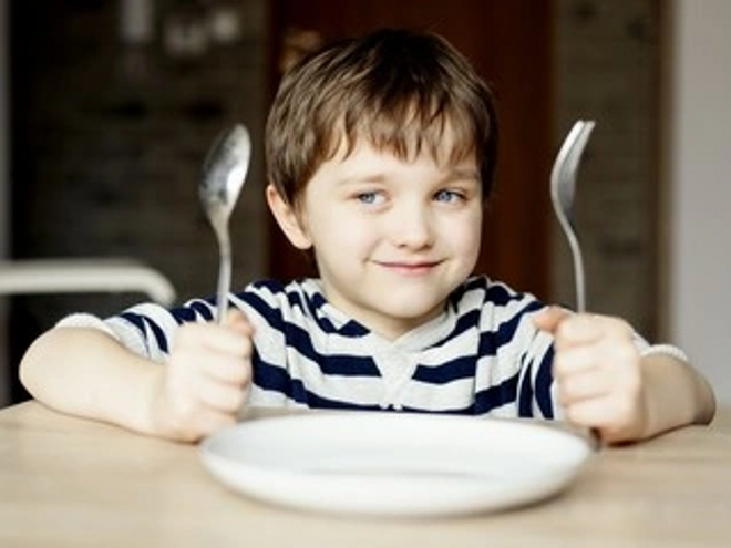 Niño alegre con sus cubiertos esperando comer alimentos constructores