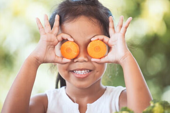 Niña cubriéndose los ojos con zanahorias