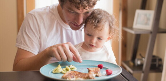 Un papá enseñándole a su bebé cuales son los alimentos constructores